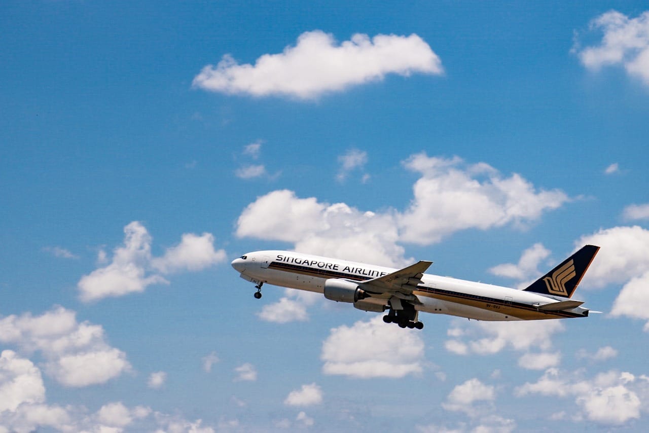 A Signapore Airlines plane flying through a blue sky with white clouds.