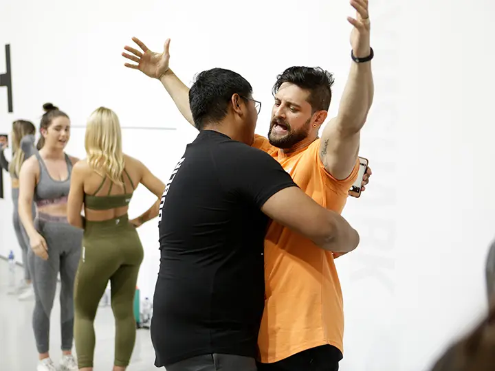 Two men in a gym hugging in celebration wearing GymShark.