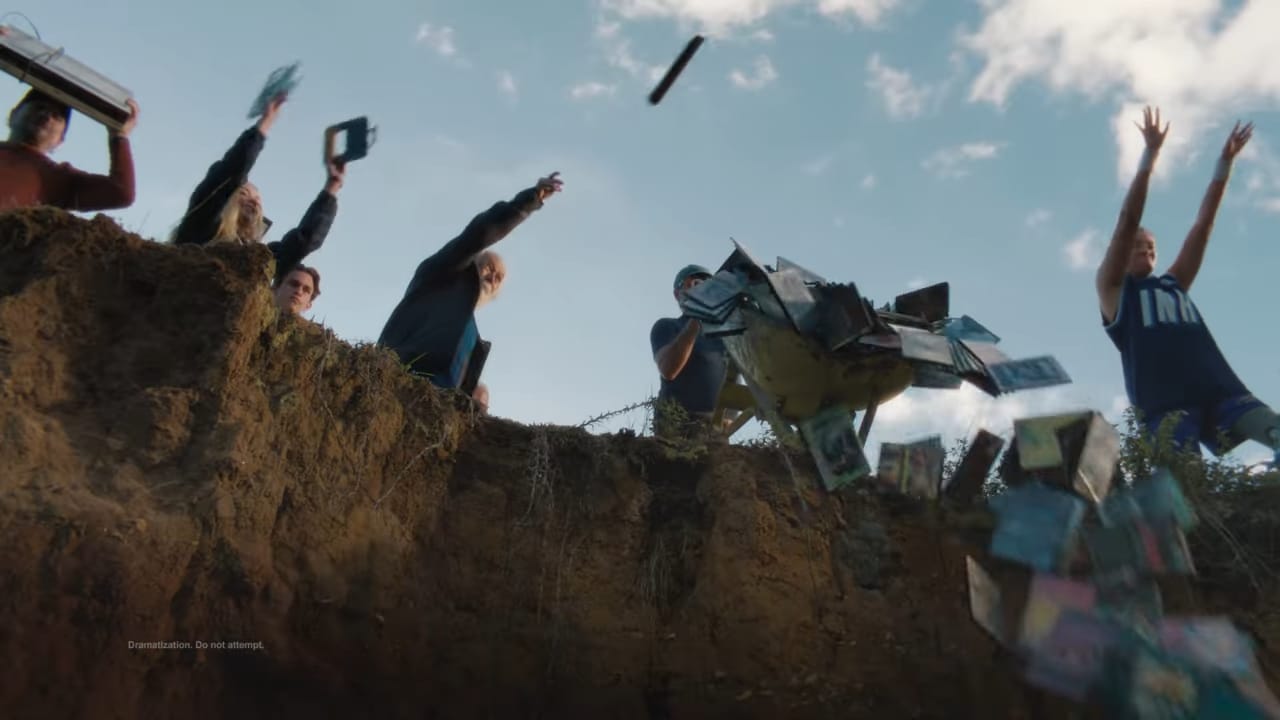 A group of people stand at the edge of a cliff, throwing cassette tapes and CDs over the edge into the air.