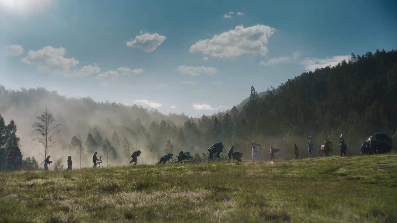 Silhouettes of people in combat poses scattered across a grassy field, with mist and trees in the background under a blue sky.